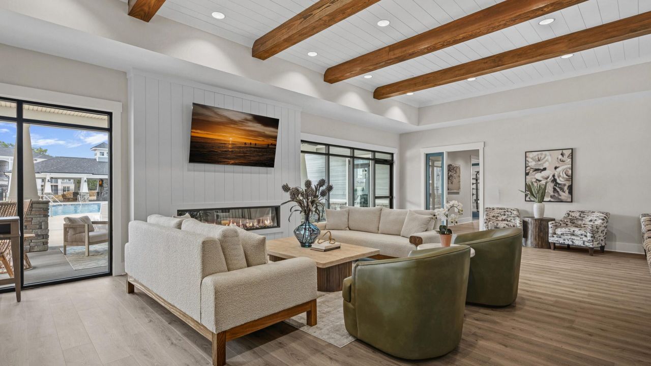 Modern living room with exposed wood beams, two sofas, green chairs, a fireplace, and a TV on the wall.
